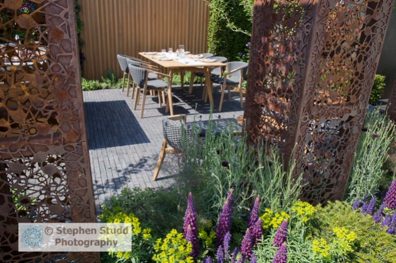 Photographer: Stephen Studd - The Urban Flow Garden: laser cut steel pillars, brick paved patio area with dining table and chairs, Lupinus 'Masterpiece' - Designer: Tony Woods - Sponsor: Thames Water