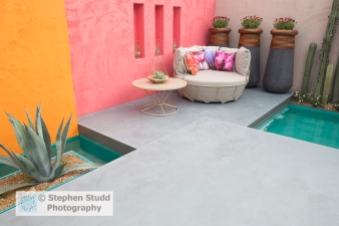 Photographer: Stephen Studd  -  Beneath A Mexican Sky garden, view of turquoise pool with Stenocereus marginatus cactus and container with Agave americana grown in gravel, orange and red, polished concrete floating patio with chair with floral prints, table with succulent growing in atrium - Designer: Manoj Malde - Sponsor: Inland Homes PLC